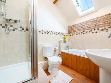 A bathroom with a shower, toilet, bathtub with wooden paneling, sink, tiled walls, skylight window, and vase with yellow flowers at Widgeon in Wheatacre