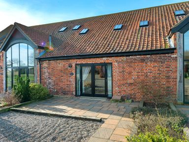 A brick building with a tiled roof and black framed glass doors and windows with paving and gravel outside at Widgeon in Wheatacre