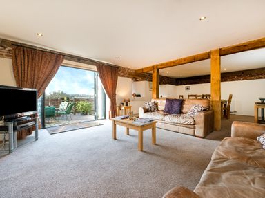 A living room with leather sofas a coffee table and a television near an open door to an outdoor patio at Teal in Wheatacre