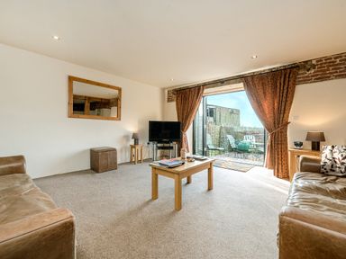 A living room with two brown leather sofas a wooden coffee table a TV on a stand and patio doors leading outside at Teal in Wheatacre