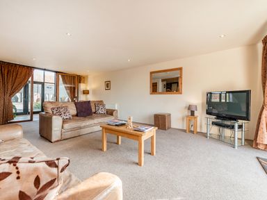 A living room with sofas a coffee table a television and large windows with curtains at Teal in Wheatacre