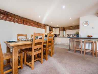 A kitchen and dining area with wooden dining table and chairs and a breakfast bar with stools at Teal in Wheatacre