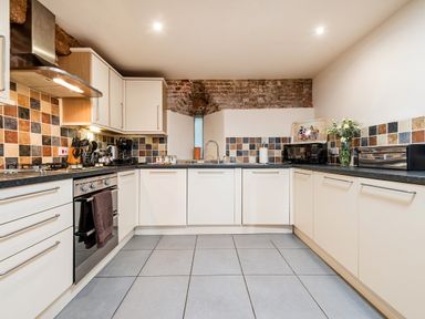 A kitchen with white cabinets gray countertops a stainless steel oven tiled backsplash and exposed brick at Teal in Wheatacre