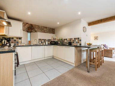 A kitchen with white cabinets a tiled floor and a breakfast bar with wooden stools at Teal in Wheatacre
