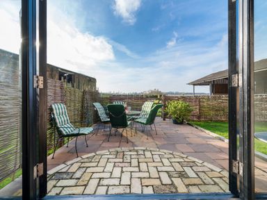 An outdoor patio with metal chairs with green and white cushions and a metal table surrounded by a wicker fence at Teal in Wheatacre
