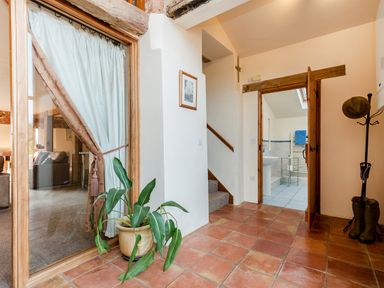 An entryway with terracotta floor tiles a potted plant a coat rack with boots and a hat a staircase and a doorway leading to a bathroom at Teal in Wheatacre