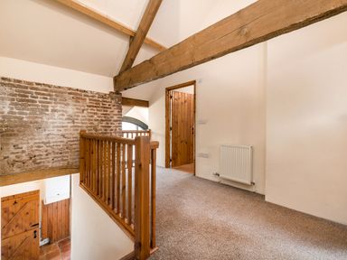 A hallway with wooden beams a brick wall and carpeted floor at Teal in Wheatacre
