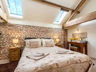 A bedroom with a double bed between two bedside tables with lamps and a dressing table with a mirror and flowers at Teal in Wheatacre