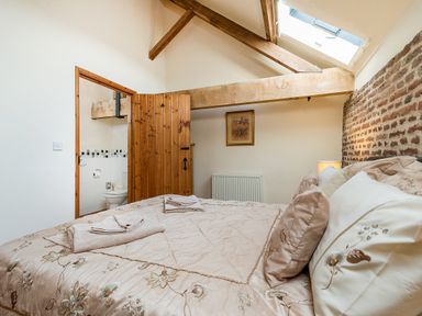 A bedroom with a bed covered in floral bedding wooden door open to a bathroom exposed wooden beams and a skylight at Teal in Wheatacre