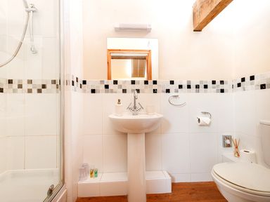 A bathroom with a pedestal sink a mirror a shower a toilet and a wooden beam at Teal in Wheatacre