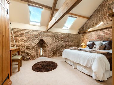 A bedroom with exposed brick walls wooden beams a double bed a wooden desk and two skylight windows at Teal in Wheatacre