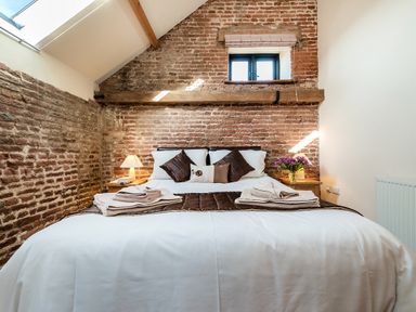 A bedroom with a bed against a brick wall with two bedside tables with lamps and flowers at Teal in Wheatacre