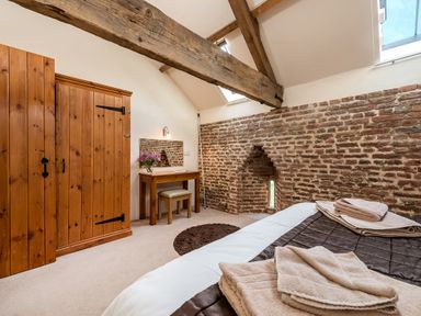 A bedroom with exposed wooden beams brick wall wooden wardrobe dressing table with mirror and bed at Teal in Wheatacre