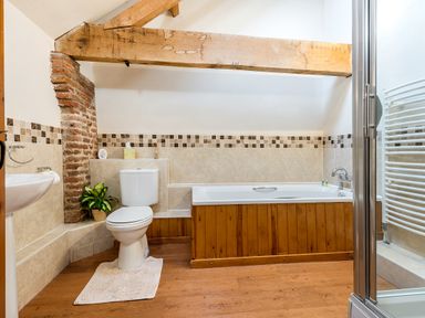 A bathroom with a toilet bathtub shower and wooden ceiling beam at Teal in Wheatacre