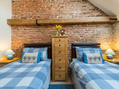 A bedroom with two single beds with blue checkered bedding a wooden chest of drawers with flowers and a teddy bear on top and exposed brick walls at Teal in Wheatacre