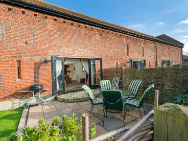 An outdoor patio area with a round table and six striped chairs next to a brick building with open double doors at Teal in Wheatacre