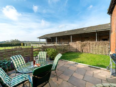 A patio with a glass table and four striped cushioned chairs next to a small lawn and wooden fencing at Teal in Wheatacre