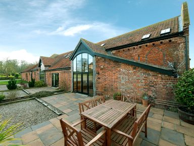 An outdoor patio with a wooden table and chairs next to a brick building with large glass doors at Teal in Wheatacre