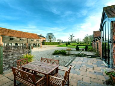 An outdoor patio with a wooden dining table and chairs next to brick and wooden buildings at Teal in Wheatacre
