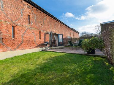 A grassy garden with a patio area and outdoor seating beside a brick building at Teal in Wheatacre