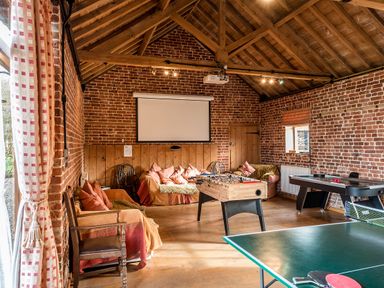 A game room with a foosball table air hockey table and ping pong table with sofas and a projector screen at Teal in Wheatacre
