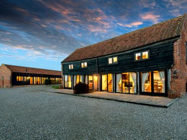 A courtyard with two rustic buildings with large windows and tiled roofs under a cloudy sky at Woodcock in Wheatacre
