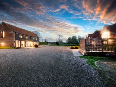 An exterior view of a brick and wood building with windows lit at dusk at Woodcock in Wheatacre