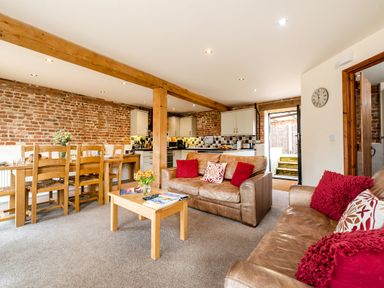 A living room and kitchen area with brown leather sofas and wooden dining table at Woodcock in Wheatacre