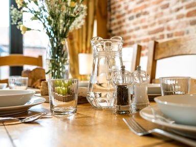 A dining table set with clear glasses plates bowls utensils a water pitcher and salt and pepper shakers at Woodcock in Wheatacre