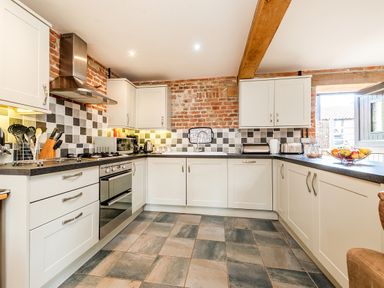 A kitchen with white cabinets black countertops a tiled floor and brick walls at Woodcock in Wheatacre