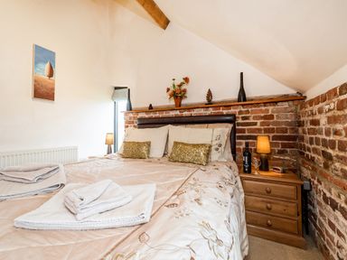 A bedroom with a double bed against a brick wall and a wooden nightstand with a lamp at Woodcock in Wheatacre