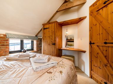 A bedroom with a bed towels wooden wardrobes a window and a dressing table at Woodcock in Wheatacre