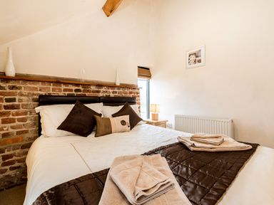A bedroom with a bed and pillows next to a brick and white wall at Woodcock in Wheatacre