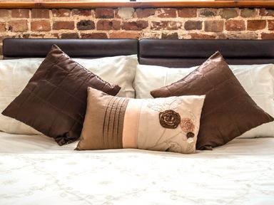 A bed with white sheets and three decorative pillows against a brick wall at Woodcock in Wheatacre