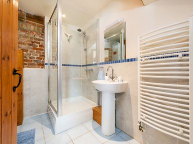 A bathroom with a glass shower enclosure a pedestal sink a towel radiator and a wooden door at Woodcock in Wheatacre