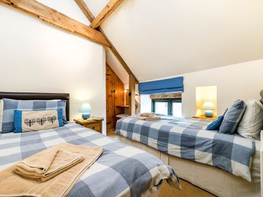 A bedroom with two single beds covered in blue and white checkered bedding with wooden beams on the ceiling at Woodcock in Wheatacre