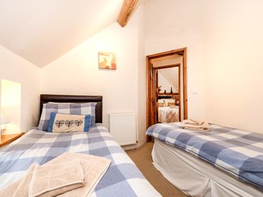 A bedroom with two single beds with blue and white checkered bedding and a doorway showing another room at Woodcock in Wheatacre