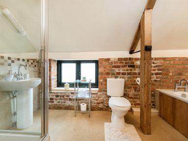 A bathroom with a toilet sink shower and bathtub with exposed brick walls and a wooden beam at Woodcock in Wheatacre