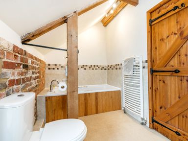 A bathroom with a toilet bathtub wooden door exposed wooden beam and a heated towel rail at Woodcock in Wheatacre