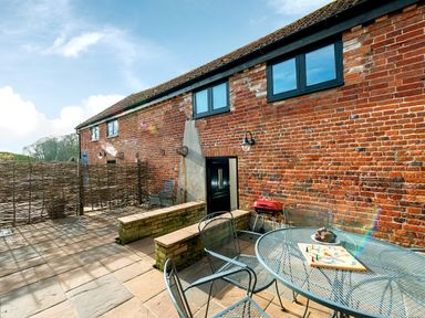 An outdoor patio with metal table and chairs a red grill and brick walls at Woodcock in Wheatacre