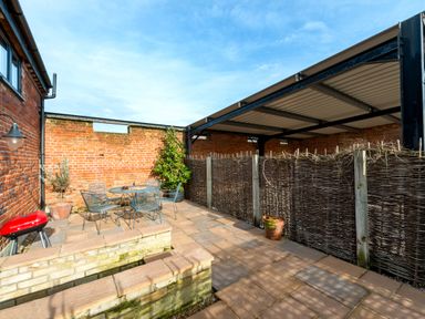 An outdoor patio area with a metal table and chairs a red barbecue and potted plants at Woodcock in Wheatacre