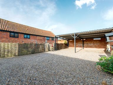 An outdoor gravel area with a metal carport and a brick building with tiled roof at Woodcock in Wheatacre