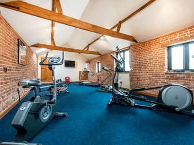 A fitness room with exercise bikes treadmills and rowing machines in a room with wooden beams and brick walls at Woodcock in Wheatacre