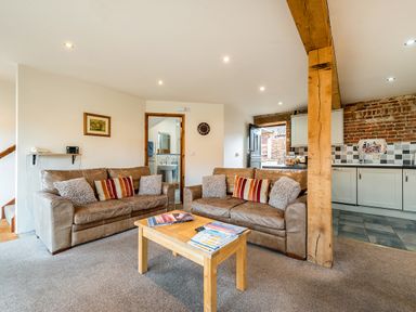 An open living room with two leather sofas and a wooden coffee table next to a kitchen with tiled backsplash at Snipe in Wheatacre