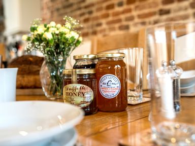 A dining table with jars of honey and marmalade flowers in a vase and drinking glasses at Snipe in Wheatacre