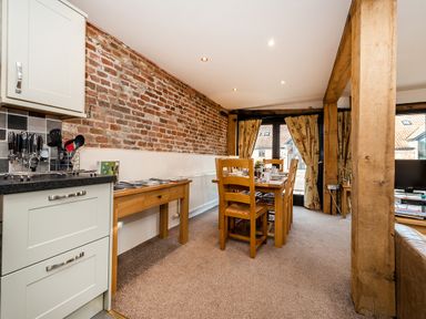 A dining area with a wooden table and chairs next to kitchen cabinets and an exposed brick wall at Snipe in Wheatacre