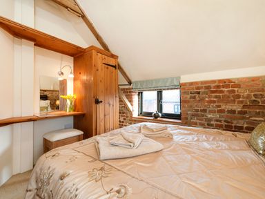A bedroom with a bed folded towels a wooden wardrobe exposed brick walls a window with a blue curtain and a wooden vanity with a mirror and flowers at Snipe in Wheatacre