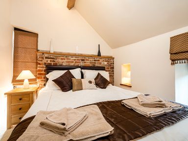 A bedroom with a double bed brown cushions and towels on the bed a wooden nightstand with a lamp and brick wall behind the bed at Snipe in Wheatacre
