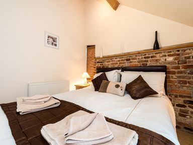 A bedroom with a bed with white and brown bedding towels on the bed a nightstand with a lamp and exposed brick wall at Snipe in Wheatacre