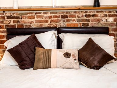 A bed with white sheets and three decorative pillows against a brick wall at Snipe in Wheatacre
